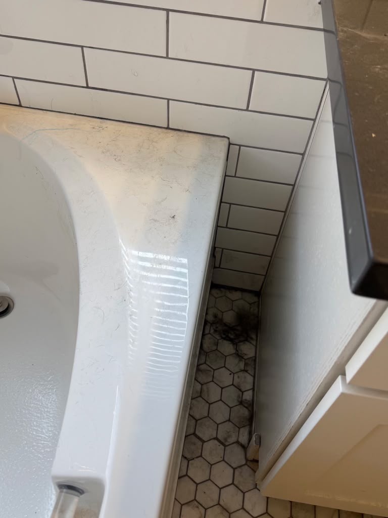 Tub edge and floor corner with dust and debris before cleaning