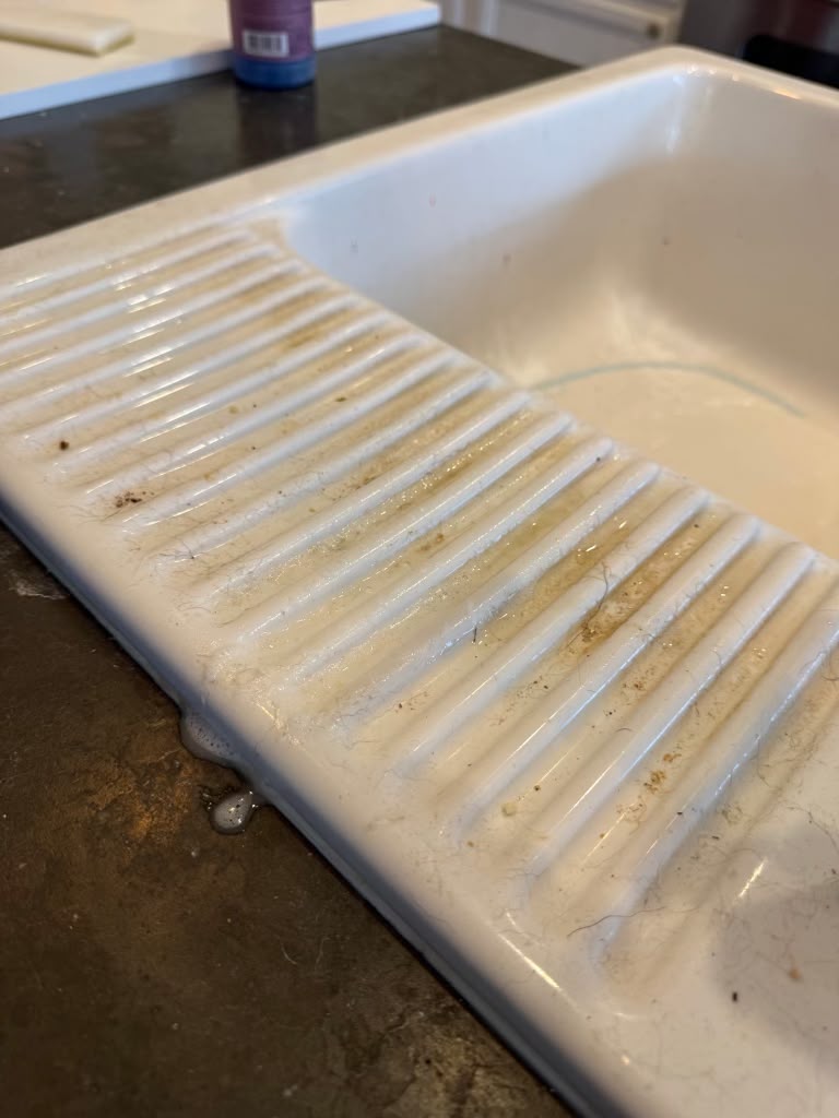 Ceramic farmhouse sink with staining and debris before cleaning